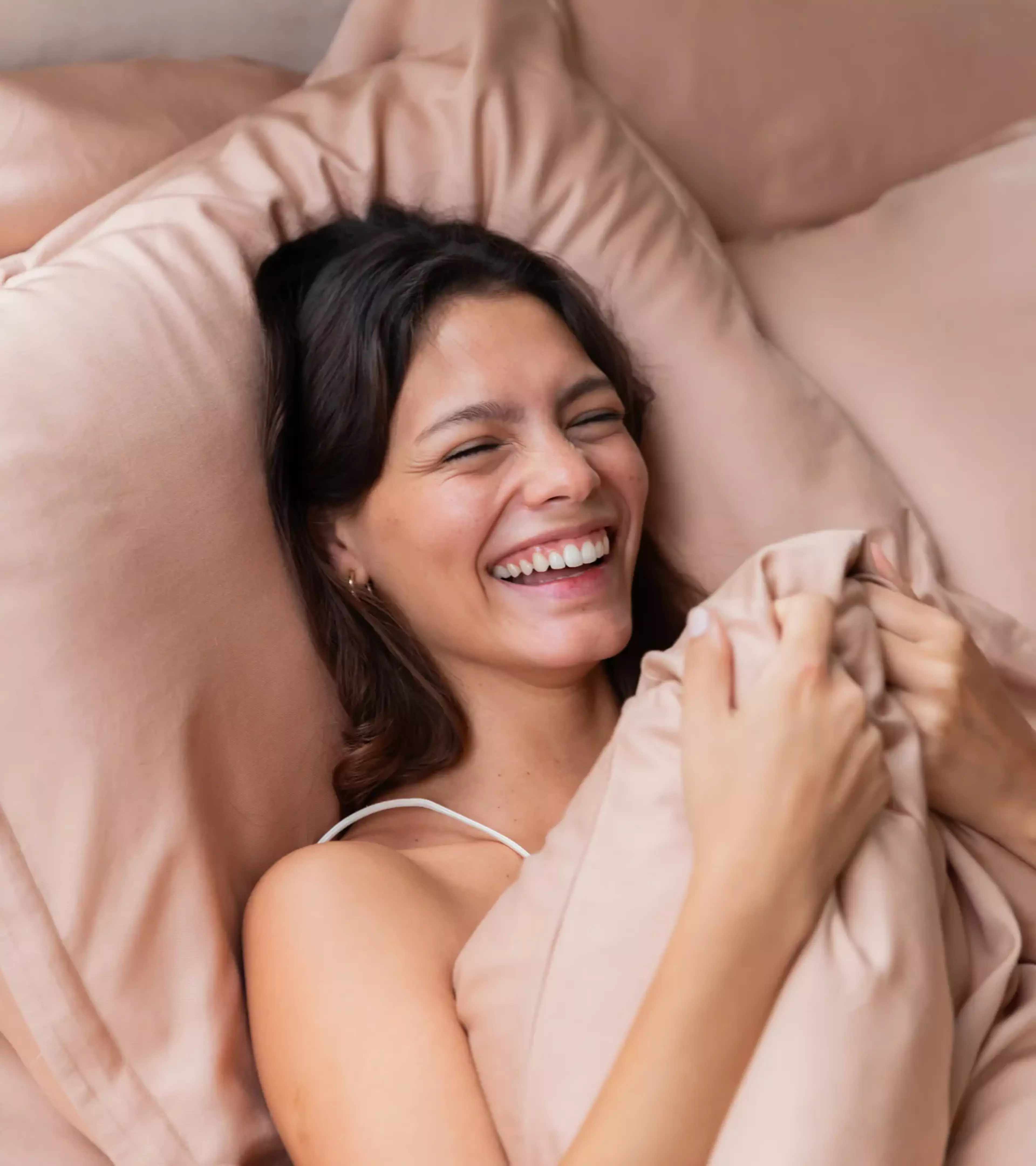 a photo of a happy woman in a bed with a pink duvet