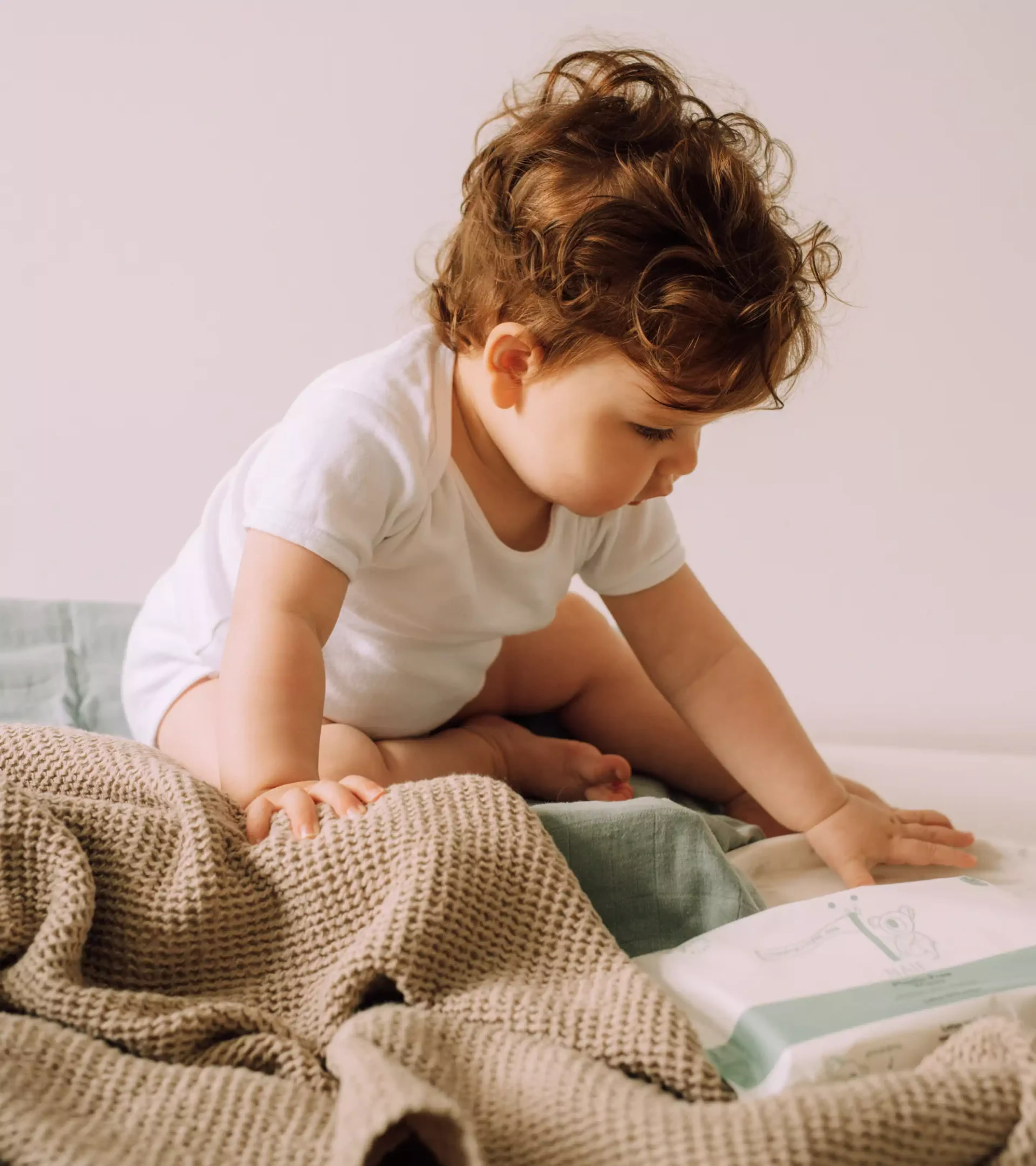 An image of a young boy playing on the bed with a plastic free wipes product next to him