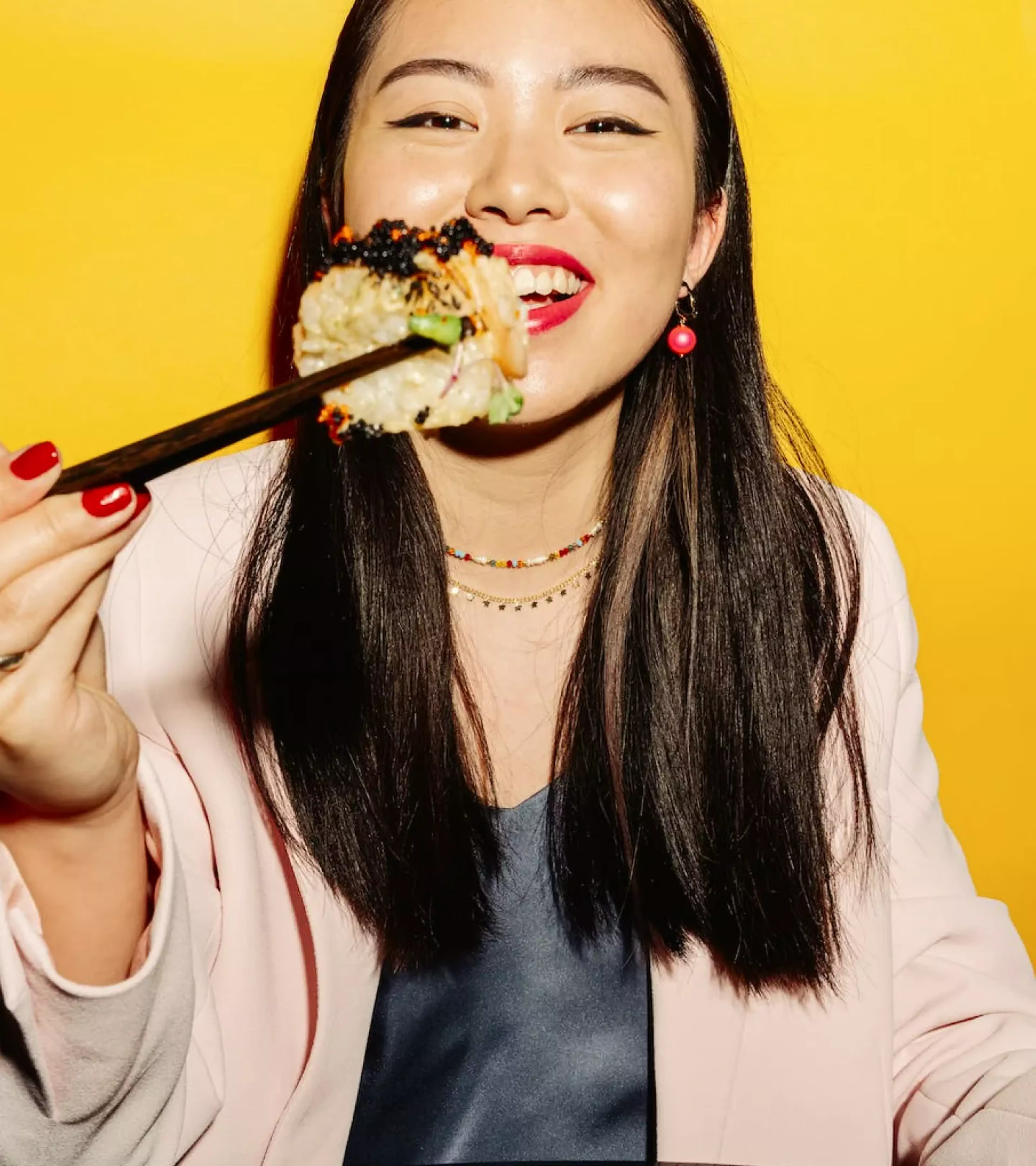 An image of a woman with dark hair eating a sushi roll