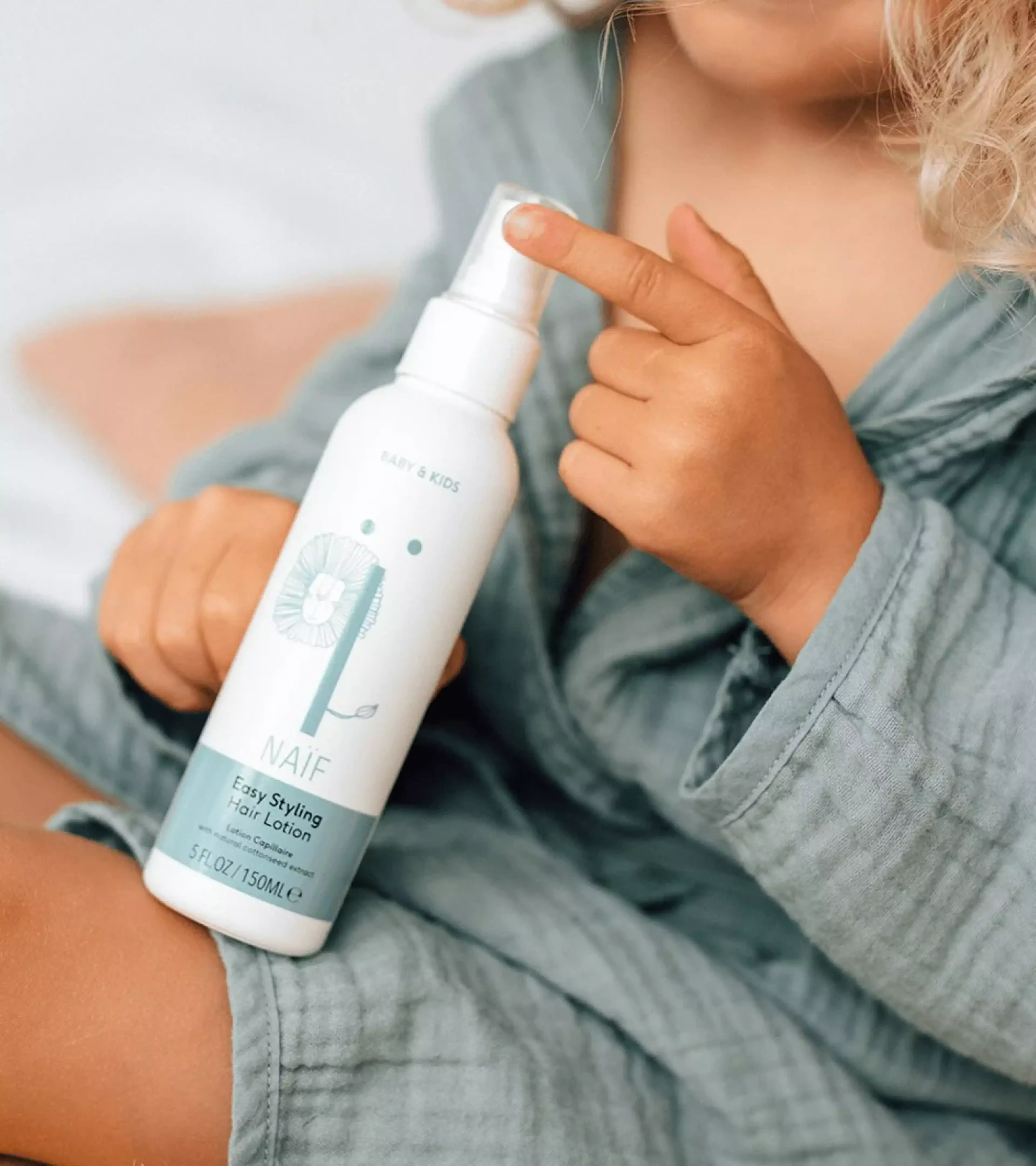 An image of a young, blond boy in a blue bathrobe holding Easy Styling Hair Lotion