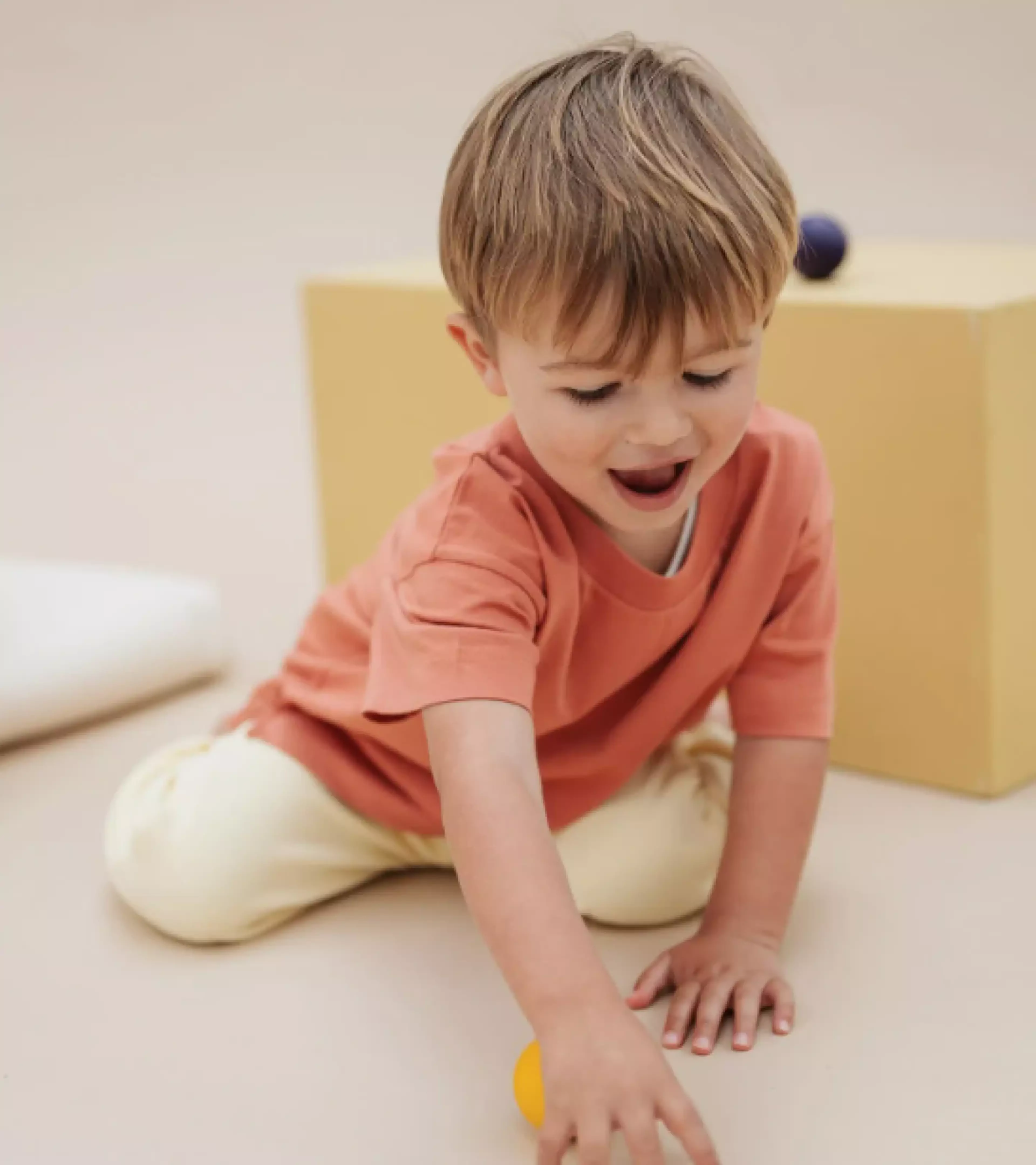 An image of a young, blond boy playing with a tiny ball