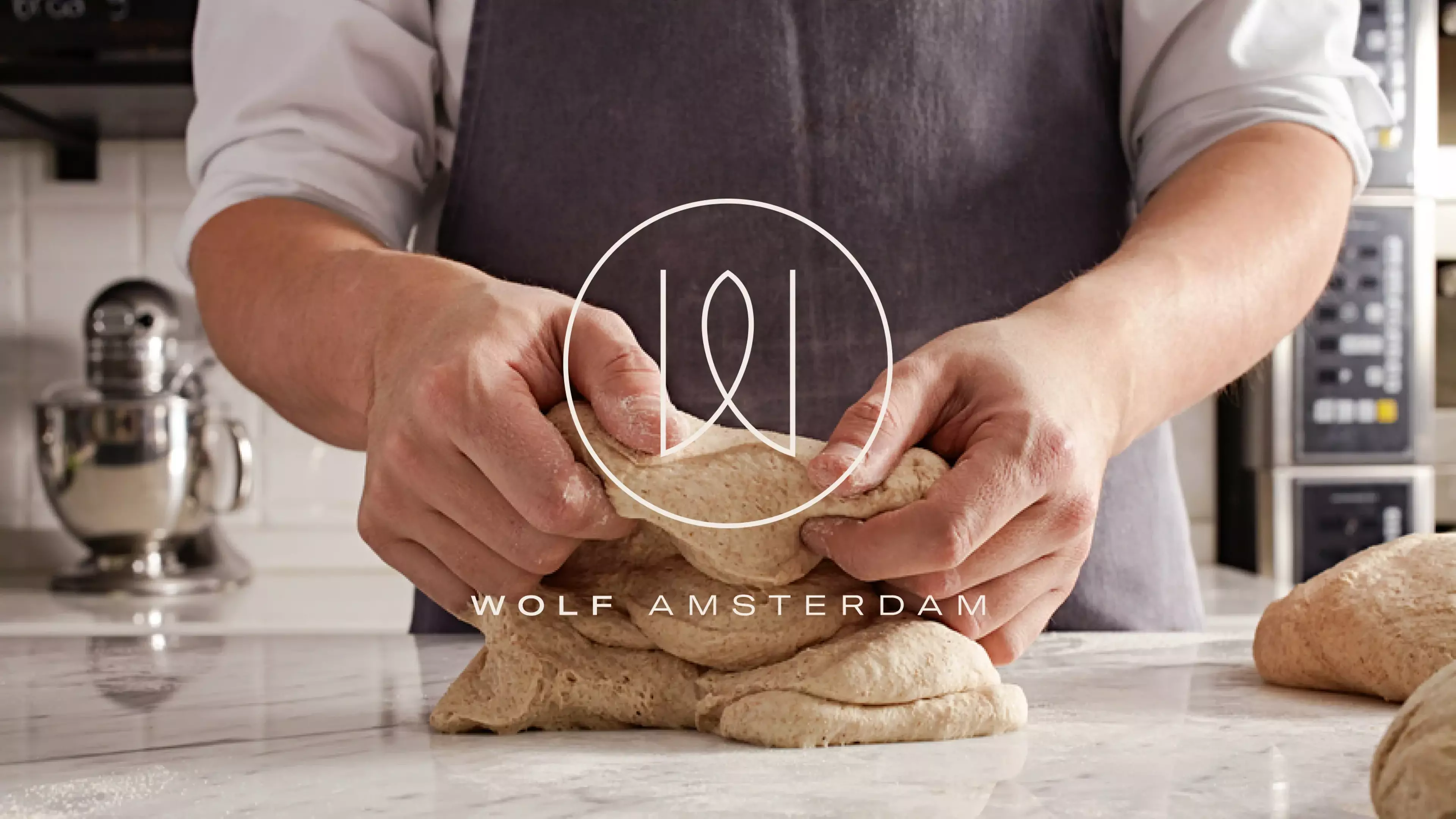 A variation of the Wolf Bakery logo with an image of a baker kneading a loaf of bread in the background